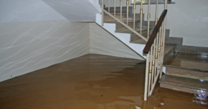 Flooded staircase with murky water covering the lower steps and pooling on the floor, walls showing water reflections. It's a stark reminder of the importance of flood prevention for home & business protection in places like Utah.